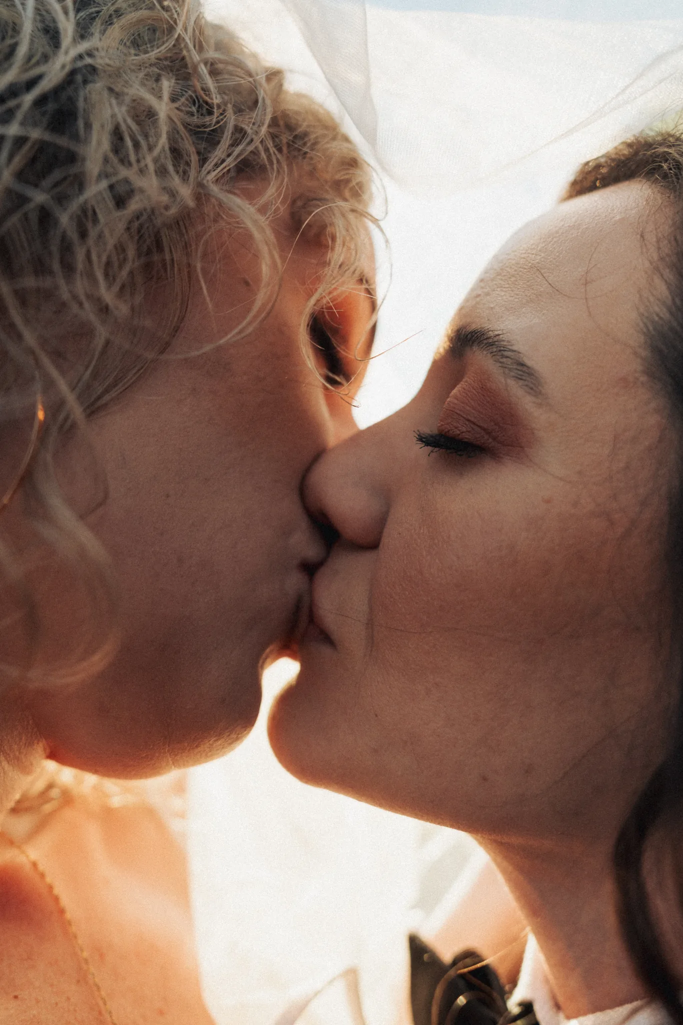 A couple kisses in golden-hour light, the sun flaring behind them