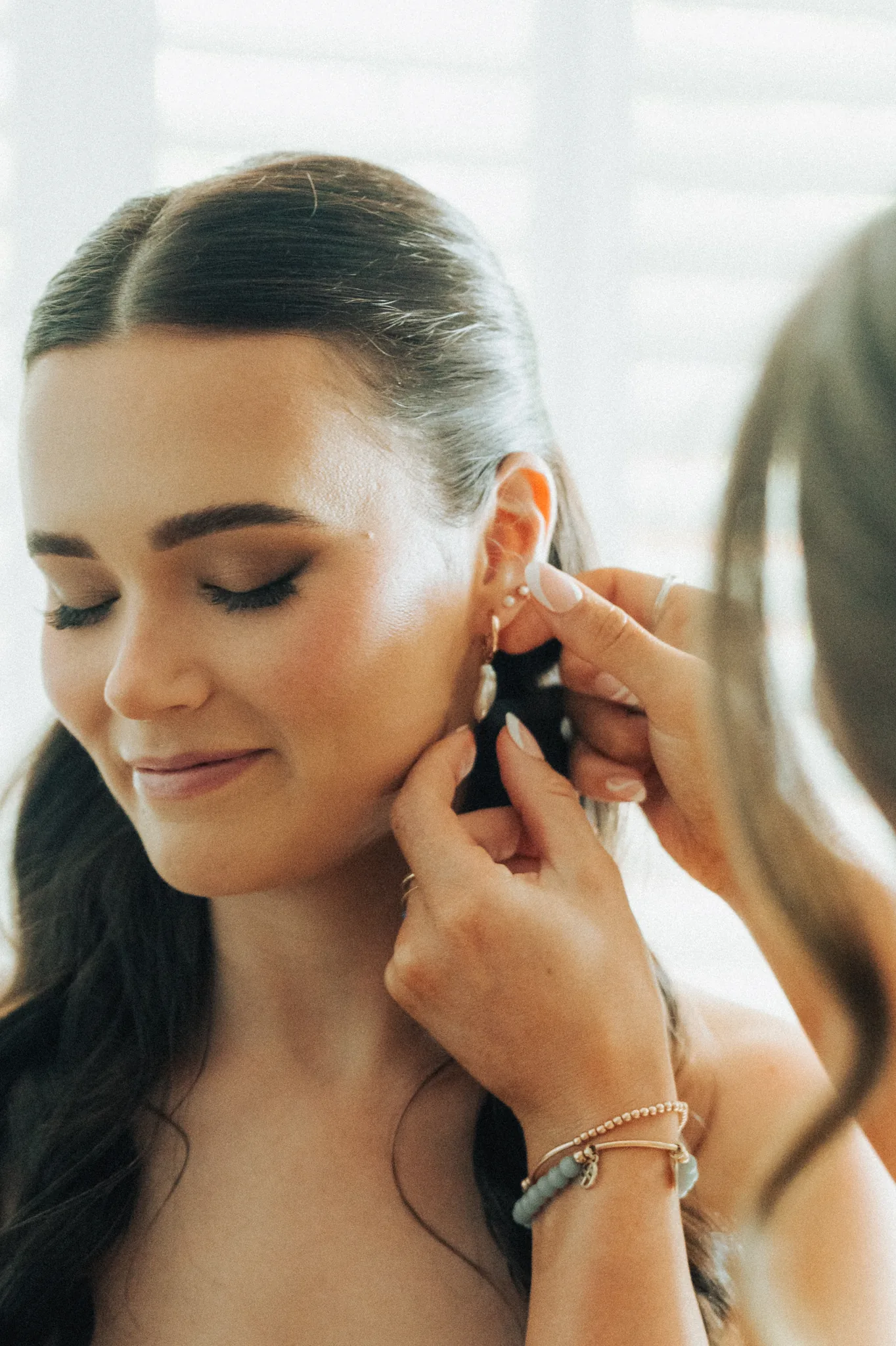 The bride fastens an earring as she gets ready, soft morning light across her face