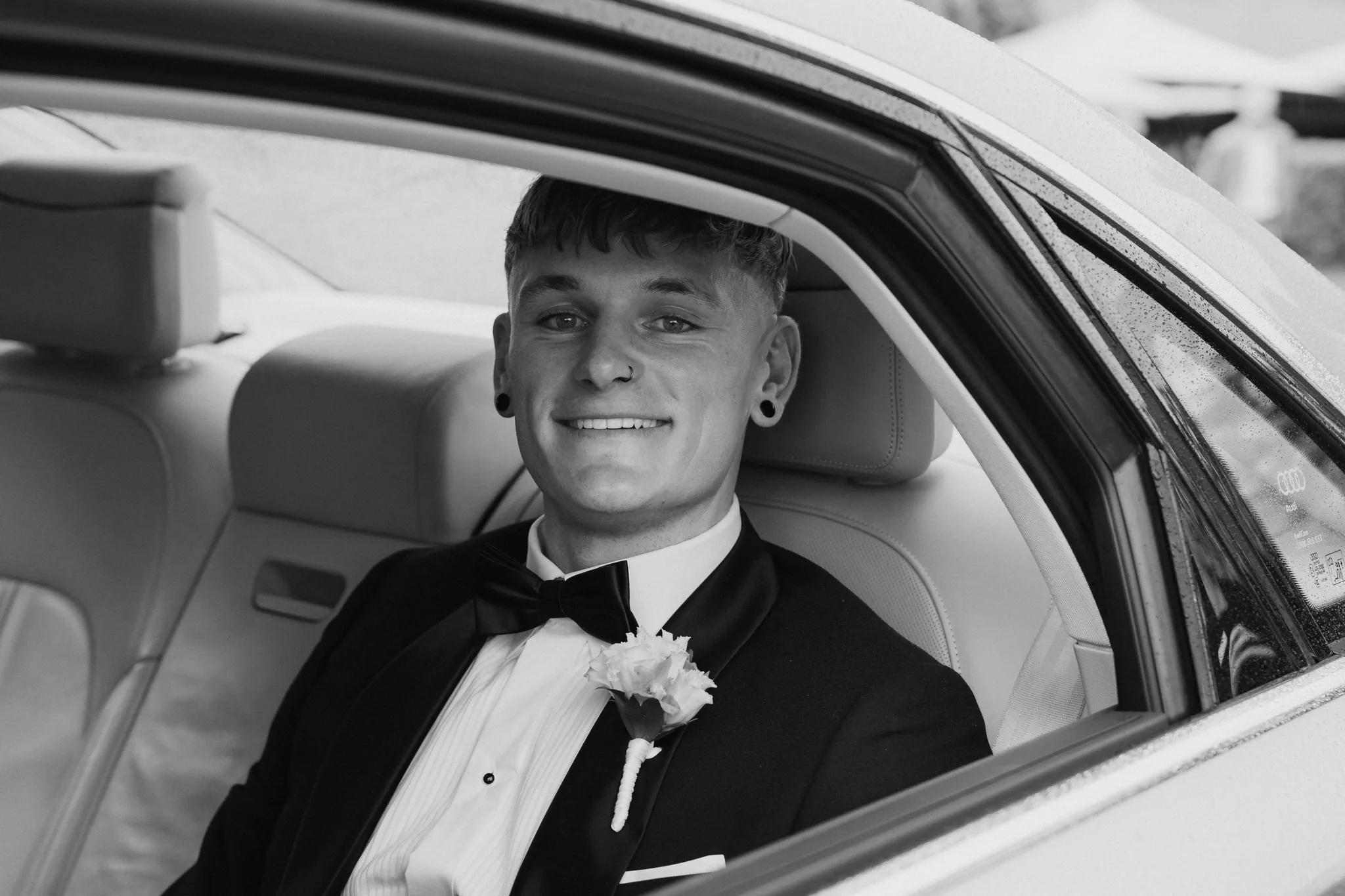The groom waits quietly by a car window before the ceremony, in black and white