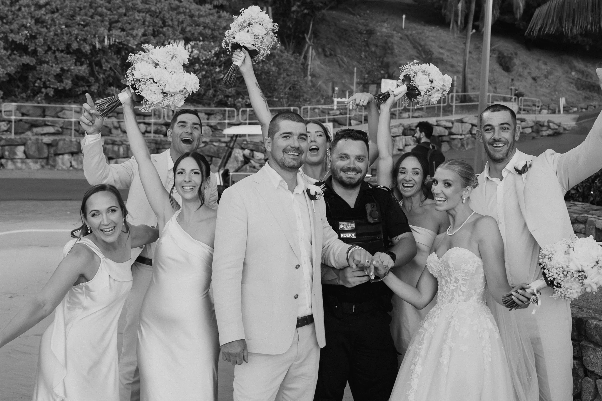 The wedding party cheers with bouquets in the air, in black and white