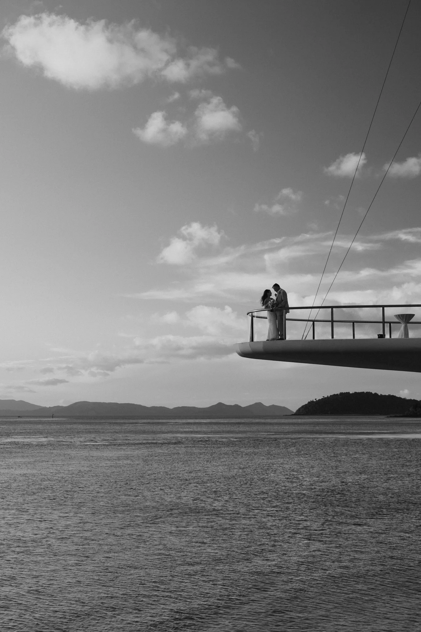 The couple as small figures on a jetty beneath a vast sky, in black and white