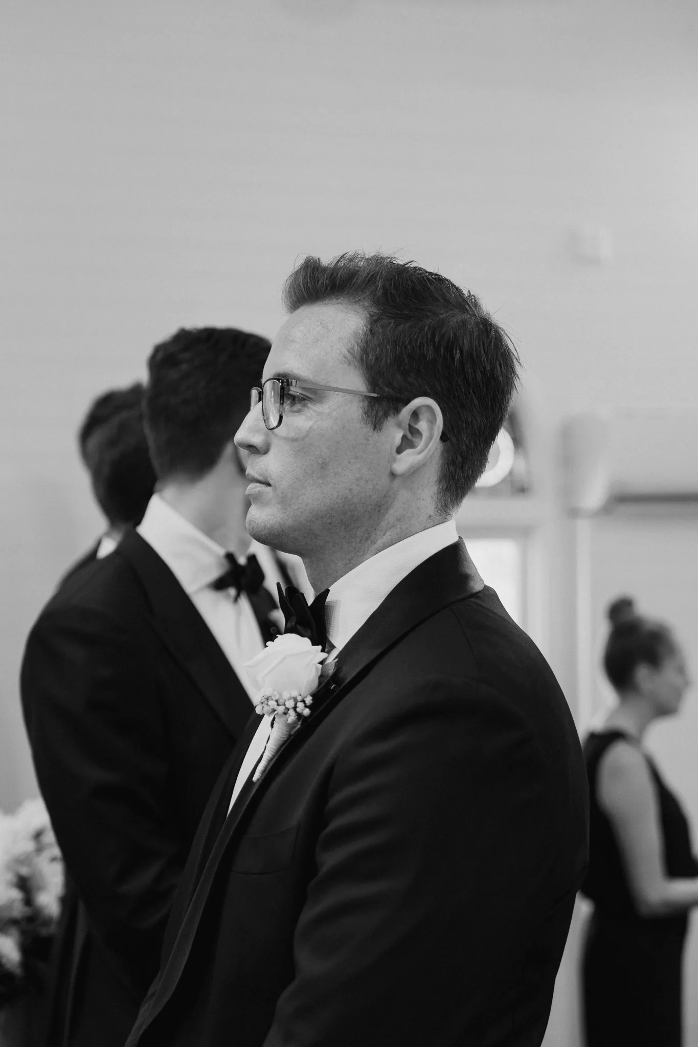 The groom kisses the bride's forehead in soft, low light, in black and white
